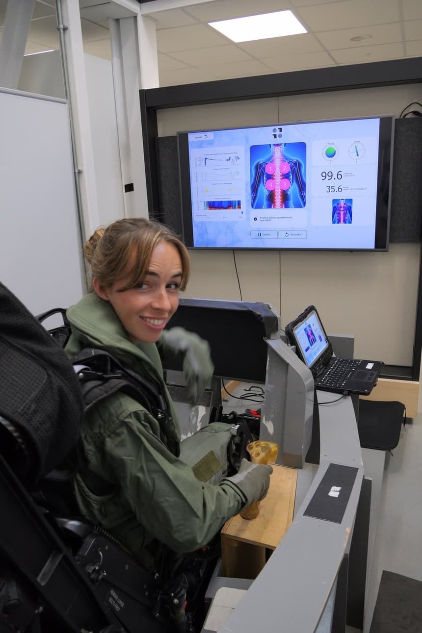 A Royal Dutch Air Force pilot in an ejection seat smiles while a screen behind her shows a body signal map